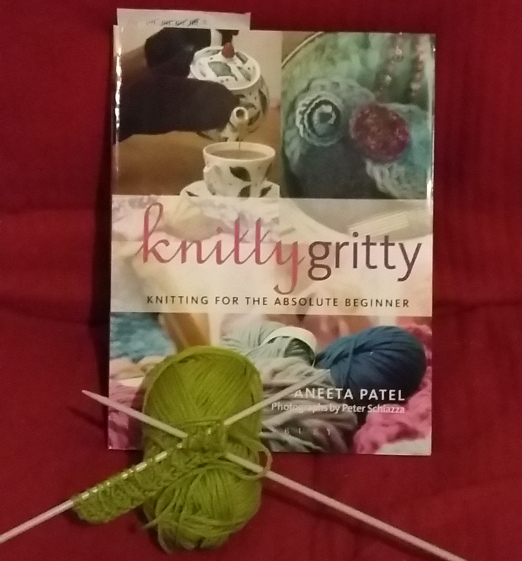 small piece on knitting on needles, with ball of wool and book 'knitty gritty'