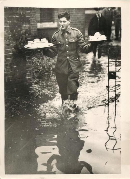1939- British soldier takes tea to comrades working to repair banks of River Ravensbourne which flooded south London.