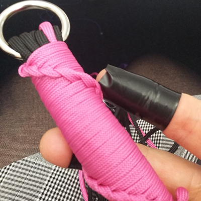 Handle of a pink and black paracord flogger made to a KinkCraft design, held in one hand. Black electrical insulation tape is wrapped round my first two fingers.